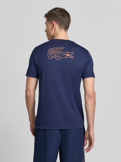 Männermodel trägt Regular Fit T-Shirt mit UV-Schutz 50+ von Lacoste Sport in Dunkelblau mit Logo-Print, unifarben, Rückansicht, Ganzkörperansicht.