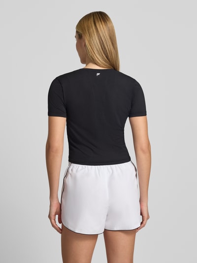 Kobiece modelka nosi czarny Damski t-shirt z elastycznej mieszanki materiałów, krój krótki, Model 'Feather' od Fabletics, okrągły dekolt, długość tyłu w rozmiarze S: 45 cm, widok całej sylwetki z tyłu