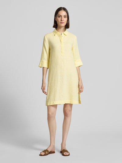 Frauenmodel trägt knielanges Hemdblusenkleid aus Leinen mit 3/4-Arm von Christian Berg Woman in Gelb, A-Linie, verdeckte Knopfleiste, Ganzkörperansicht von vorne.