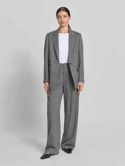 Kobiece modelka nosi Relaxed Fit Blazer mit Pattentaschen Modell 'GLENDALE' od Drykorn, szary materiał z domieszką wiskozy, krój relaxed fit, klapy, patki, zapięcie na guzik, długość tyłu w rozmiarze 36: 72 cm, szerokość w rozmiarze 36: 33 cm, długość rękawa w rozmiarze 36: 60 cm, widok całej sylwetki z przodu.