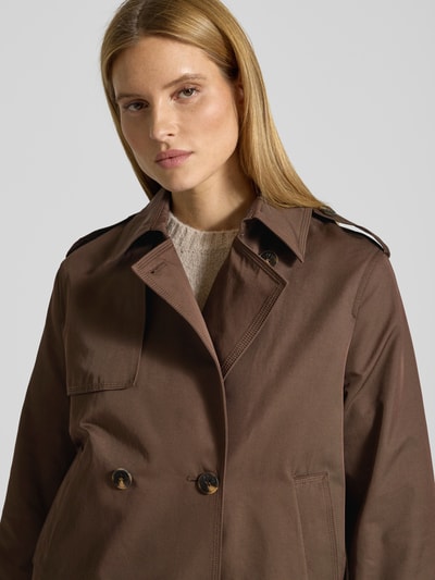 Modelka kobieca nosi Trenchcoat in kurzem Design mit Baumwoll-Anteil od Jake*s Casual, brązowy, prosty krój, widoczne kieszenie, detalowe guziki, bawełniany miks materiałów, widok z przodu, zbliżenie na górną część ciała.