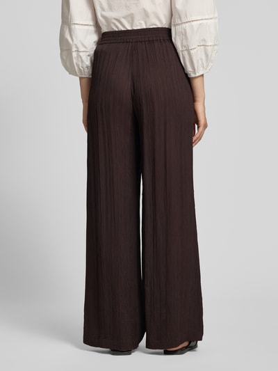 Frauenmodel trägt Wide-Leg-Pants aus Reine Viskose mit elastischem Bund von Someday, dunkelbraun, Loose-Fit, Ganzkörperansicht Rückansicht. Modell 'Cenya resort', Bundweite bei Größe 36: 39 cm, Innenbeinlänge: 81 cm.