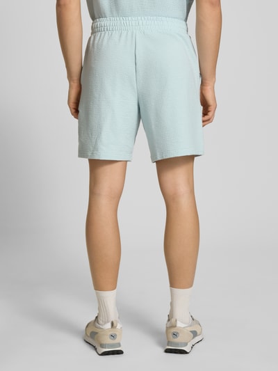 Männermodel trägt Shorts mit Logo-Stitching von PUMA PERFORMANCE in Hellblau mit Strukturmuster, elastischem Bund, Ganzkörperansicht Rückansicht.