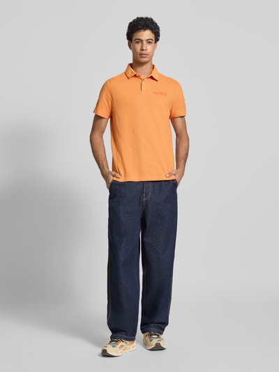 Männermodel trägt Regular Fit Poloshirt aus reiner Baumwolle von Replay in Orange, Polokragen, Label-Stitching, kurzärmelig, Ganzkörperansicht von vorne.