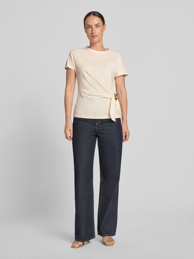 Frauenmodel trägt T-Shirt in Wickel-Optik mit Brosche von Christian Berg Woman Selection aus reiner Baumwolle, Regular Fit, Ganzkörperansicht von vorne.
