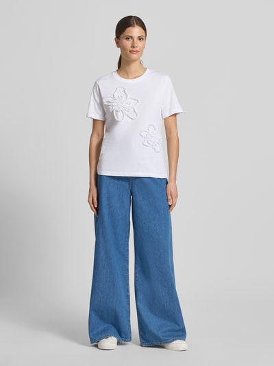 Frauenmodel trägt Regular Fit T-Shirt mit Rüschenbesatz von Comma aus Reine Baumwolle, Rundhalsausschnitt, Damen T-Shirt, Größe 36, Rückenlänge 56 cm, Weiß, kombiniert mit blauer weiter Jeans, glatter Stoff, Ganzkörperansicht von vorne.