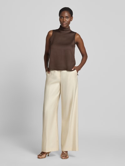 Frauenmodel trägt Blusentop mit Stretch-Anteil von DRYKORN in Braun, ärmellos, Satin, Rollkragen, verlängerte Rückseite, Ganzkörperansicht von vorne.