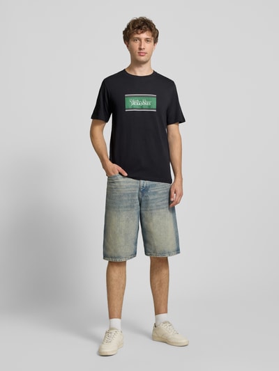 Männermodel trägt Regular Fit T-Shirt mit Logo-Print Modell 'Buster' von JACK & JONES in Schwarz, reine Baumwolle, Ganzkörperansicht von vorne.