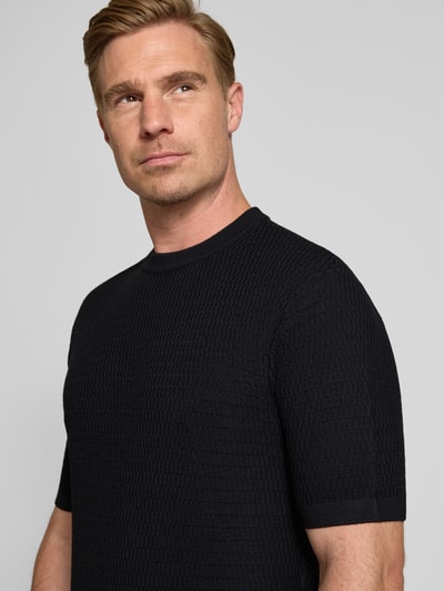 Männermodel trägt Slim Fit Strickshirt aus reiner Wolle von Emporio Armani, schwarz, Kurzarm, strukturierte Oberfläche, Nahaufnahme Oberkörper.
