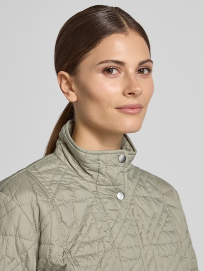 Frauenmodel trägt Steppjacke mit Stehkragen und Eingrifftaschen von Fuchs Schmitt, dezente grüne Farbe, Nahaufnahme Oberkörper, Regular Fit, Knopfleiste, Rückenlänge bei Größe 36: 64 cm, Schulterbreite: 43 cm, Brustweite: 49 cm, Ärmellänge: 65 cm.