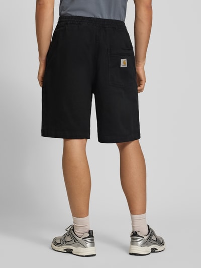 Mannenmodel draagt Shorts uit katoenmix Model 'Floyde' van Carhartt Work In Progress, zwart, relaxed fit, steekzakken, elastische band met tunnelkoord, zij- en achterzakken, mix van katoen en elastaan, bandwijdte maat M 39 cm, binnenbeenlengte maat M 25 cm, geheel achteraanzicht.