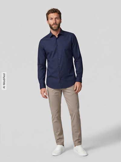 Männermodel trägt dunkelblaues Slim Fit Businesshemd mit Kentkragen von Jake*s, beige Hose, glatter Stoff, Ganzkörperansicht von vorne, KI-modifiziertes Bild.