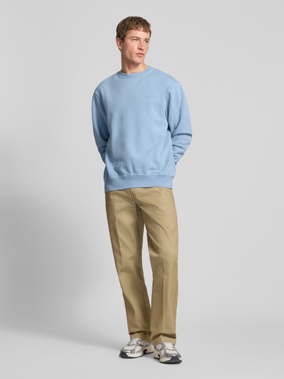 Mannenmodel draagt 'Sweatshirt mit Label-Stitching und Rundhalsausschnitt' van Dickies, lichtblauw, relaxed fit, katoenmix, label-stitching, ronde hals, ruglengte maat M 69 cm, mouwlengte maat M 68 cm, full body frontaal.