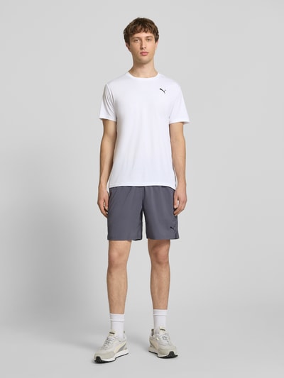 Männermodel trägt TRAINING T-Shirt mit Label-Detail Modell von PUMA PERFORMANCE, weiß, Gerader-Schnitt, Rundhalsausschnitt, Ganzkörperansicht von vorne. Herren T-Shirt, Kurzärmeliges Design, Rückenlänge bei Größe M: 73 cm.