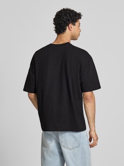 Männermodel trägt Relaxed Fit T-Shirt mit Logo-Print von REVIEW aus reiner Baumwolle, Halbarm, Rundhalsausschnitt, Rückenlänge 68 cm, Ganzkörperansicht Rückansicht.