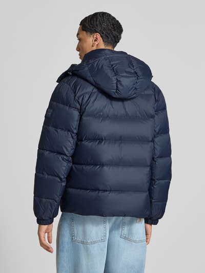 Männermodel trägt Regular Fit Steppjacke mit abnehmbarer Kapuze von Calvin Klein Jeans in Dunkelblau, glatte Textur, Ganzkörperansicht Rückansicht.