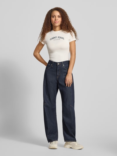 Vrouwenmodel draagt effen kleuren Slim Fit T-shirt uit katoenmix Model 'SLIM VARSITY' van Tommy Jeans met labelprint, ronde hals, korte mouw, voorkant volledig zichtbaar, Ganzkörperansicht von vorne.