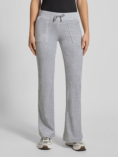 Frauenmodel trägt Low Rise Sweatpants mit elastischem Bund Modell 'LAYLA' von Juicy Couture aus grauem Baumwoll-Mix mit Stretch-Anteil, Flared-Cut, Eingrifftaschen, Innenbeinlänge 39 cm, Ganzkörperansicht von vorne.
