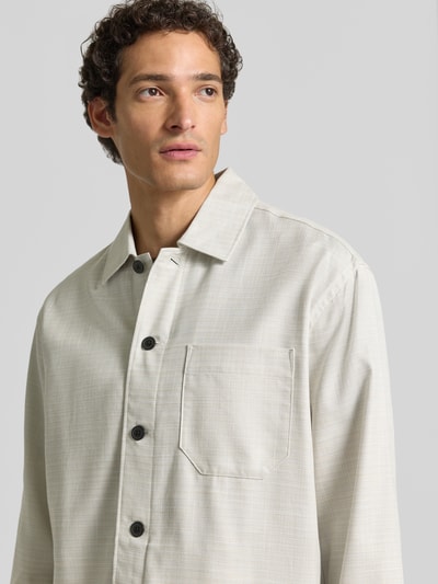 Mężczyznamodel nosi koszulę wierzchnią Relaxed Fit Overshirt aus reiner Baumwolle model 'HENRY' od Selected Homme, jasnoszara z czarnymi guzikami, gładka tekstura, zbliżenie na górną część ciała, widok z przodu.