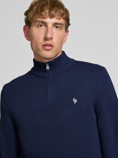 Männermodel trägt dunkelblauen Slim Fit Strickpullover aus reine Baumwolle von REVIEW mit Label-Stickerei, Nahaufnahme Oberkörper.