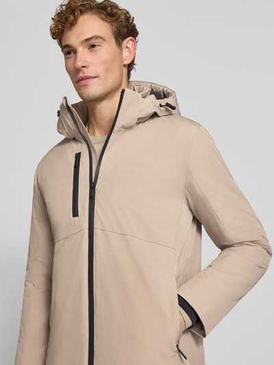 Męski model nosi Regular Fit Parka mit Logo-Print od Lindbergh z elastycznej mieszanki materiałów, beżowy kolor, przód z zamkiem, napoleońska kieszeń, kaptur z tunelem, długość tyłu 90 cm, szerokość ramion w rozmiarze M: 50 cm, szerokość w klatce piersiowej w rozmiarze M: 58 cm, długość rękawów 65 cm, nahaufnahme górnej części ciała.