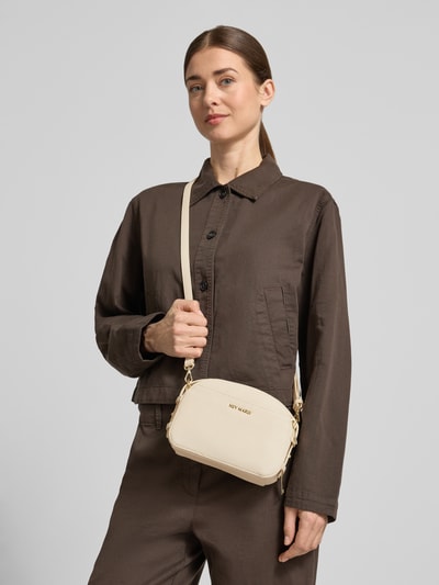 Frauenmodel trägt Umhängetasche mit Label-Detail Modell 'Style Mate' von Hey Marly in Beige, Hauptfach mit Reißverschluss, Verstellbarer Schultergurt, Reißverschlussfach innen, Breite 21 cm, Länge 15 cm, Tiefe 8 cm, Länge Schulterriemen 44 cm, Ganzkörperansicht von vorne.