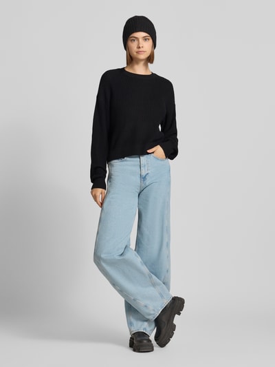 Modelka nosi Relaxed Fit Pullover aus Baumwoll-Mix Modell 'Maysa' von NOISY MAY®, czarny sweter o fakturze dzianiny, okrągły dekolt, damski pulower, długość tyłu w rozmiarze S: 50 cm, długość rękawa w rozmiarze S: 59 cm, widok całej sylwetki z przodu