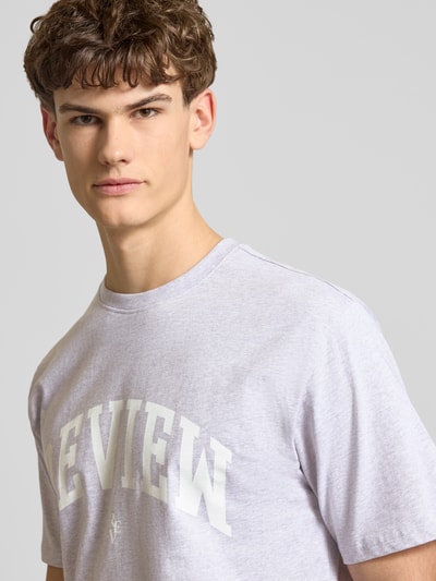 Männermodel trägt T-Shirt mit Label-Print und Rundhalsausschnitt von REVIEW in Hellgrau, reine Baumwolle, Regular Fit, Nahaufnahme Oberkörper.