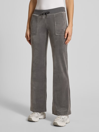 Frauenmodel trägt Low Rise Sweatpants mit elastischem Bund Modell 'LAYLA' von Juicy Couture aus grauem Baumwoll-Mix mit Stretch-Anteil, Flared-Cut, Eingrifftaschen, Ganzkörperansicht von vorne.