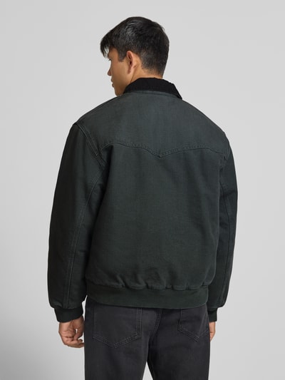 Männermodel trägt Jacke mit Reißverschluss und Label-Detail Modell 'Santa Fe' von Carhartt Work In Progress in Dunkelgrün, Baumwolle, Ganzkörperansicht Rückansicht. Regular Fit, Umlegekragen, sichtbare Textur und Nähte, KI-modifiziertes Bild.