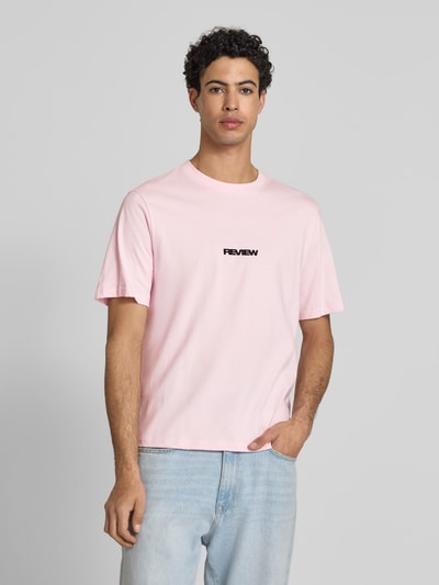 Męski model trägt T-Shirt mit Logo und Rundhalsausschnitt von REVIEW z czystej bawełny, krój relaxed fit, długość tyłu w rozmiarze M: 68 cm, jasnoróżowy, prostokątny fason, gładka faktura, całkowity widok z przodu.