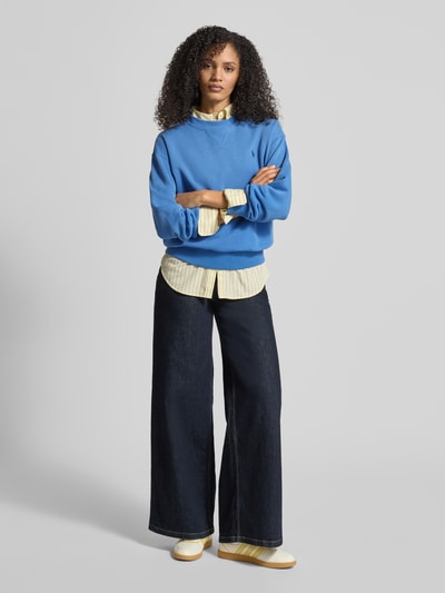 Frauenmodel trägt Bluza z wyhaftowanym logo Sweatshirt mit Label-Stitching von Polo Ralph Lauren, mieszanka bawełny, luźny krój, prążkowane wykończenia, okrągły dekolt, widoczne faktury materiału, kolory niebieski i żółty, Ganzkörperansicht von vorne.
