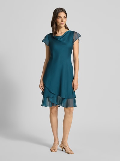 Modelka nosi knielanges Cocktailkleid mit Wasserfall-Ausschnitt von Christian Berg Cocktail, szmaragdowy, szyfon, A-linia, długość do kolan, widok całej sylwetki z przodu.
