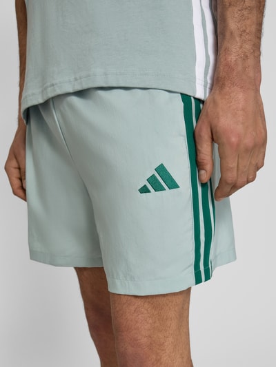 Mężczyzna nosi Regular Fit Sport-Shorts mit Kontraststreifen Modell 'CHELSEA' od adidas Sportswear w kolorze jednolitym z logo, elastycznym pasem i bocznymi kieszeniami, detal z kontrastowymi paskami, krój regular fit, zbliżenie na górną część nóg.