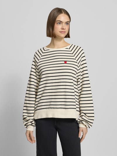 Frauenmodel trägt Oversized Sweatshirt aus Baumwoll-Mix Modell 'GRETA' von Pieces, cremefarben mit schwarzen Streifen, Rundhals, rote Herz-Applikation, unifarbene Two Tone Optik, lange Ärmel mit Rippbündchen, lockere Passform, Nahaufnahme Oberkörper.