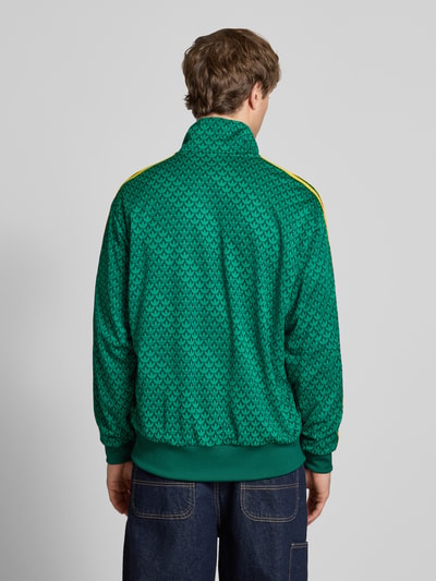 Männermodel trägt Slim Fit Jacke mit Stehkragen Modell 'Firebird' von adidas Originals in Grün mit gelben Streifen und Logo-Stitching, elastische Abschlüsse, Rückansicht, Ganzkörperansicht