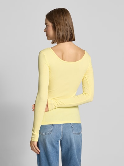 Kobiece model prezentuje Slim Fit Langarmshirt aus Baumwoll-Mix Modell 'KITTE' od Pieces w żółtym kolorze, prążkowana tekstura, widok całej sylwetki z tyłu.