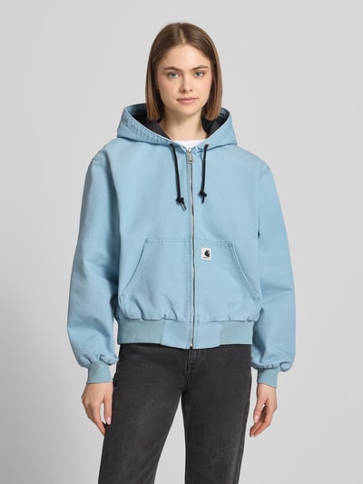 Frauenmodel trägt Sweatjacke mit Kapuze und Känguru-Tasche von Carhartt Work In Progress in Hellblau, Reine Baumwolle, Relaxed-Fit mit Label-Detail sowie Reißverschluss, Känguru-Tasche und Rippbündchen, Ganzkörperansicht von vorne. Rückenlänge 59 cm, Schulterbreite 52 cm, Brustweite 58 cm, Ärmellänge 60 cm bei Größe S.
