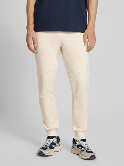Männermodel trägt Regular Fit Sweatpants mit Label-Applikation von Balr. in Beige aus Baumwoll-Mix, Ganzkörperansicht von vorne.