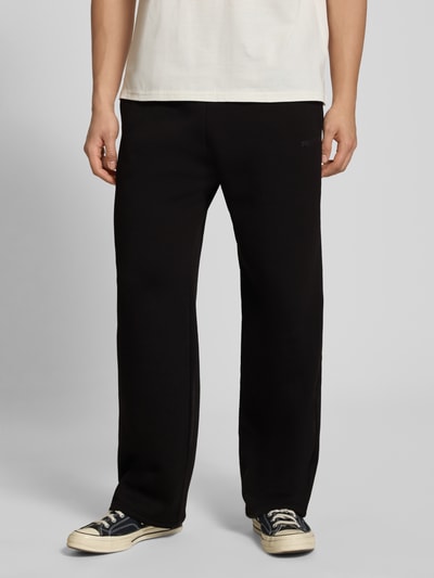 Männermodel trägt Sweatpants mit Logo-Print und Gesäßtasche von REVIEW, Schwarz, Baumwoll-Mix, Gerader-Schnitt, Eingrifftaschen, Nahaufnahme Unterkörper, ganz leicht von vorne.