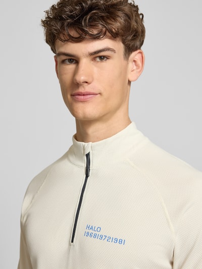Mannenmodel draagt Longsleeve met Stehkragen und Reißverschluss Modell 'SORONA' van HALO, regular fit, labelprint, lichtcrème met blauwe tekst, structuurstof, Nahaufnahme bovenlichaam.