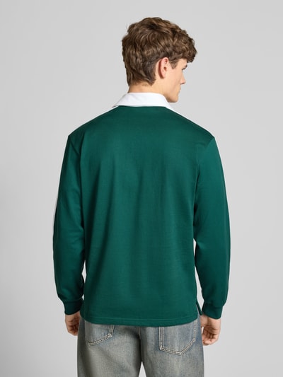 Männermodel trägt Poloshirt mit kurzer Knopfleiste von adidas Originals in Grün mit weißem Kragen aus reiner Baumwolle, Regular Fit, Ganzkörperansicht Rückansicht.