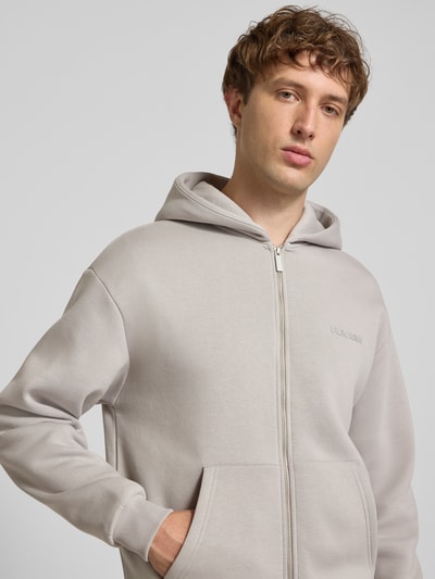 Männermodel trägt Regular Fit Sweatjacke mit Känguru-Tasche von REVIEW aus Baumwoll-Mix in Hellgrau, Nahaufnahme Oberkörper.