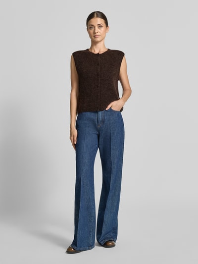 Frauenmodel trägt Regular Fit Cardigan aus elastischem Alpaka-Mix mit Knopfleiste von MOS MOSH, brauner Farbton und melierte Textur, ärmelloses Design, kombiniert mit blauen Jeans, Ganzkörperansicht von vorne.