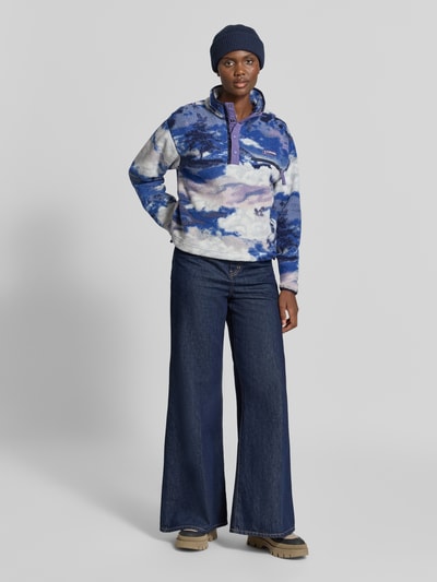 Vrouwenmodel draagt Fleeceshirt met opstaande kraag en labelpatch Model 'Helvetia II' van Columbia in blauw-paars Fleece, straight fit, borstzak met ritssluiting, voorkant, Ganzkörperansicht von vorne. Ruglengte maat S: 57 cm, schouderbreedte: 48 cm, borstwijdte: 54 cm, mouwlengte: 59 cm.