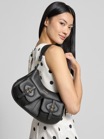 Frauenmodel trägt Shoulder Bag mit Logo-Detail Modell 'Mavery' von Coccinelle, Schwarz mit goldfarbenem Akzent, Nahaufnahme Oberkörper, Damen Shoulder Bag von Coccinelle, Hauptfach mit Reißverschluss, Schulterriemen, Breite 22 cm, Länge 21 cm, Tiefe 6 cm, Länge Schulterriemen 73 cm.