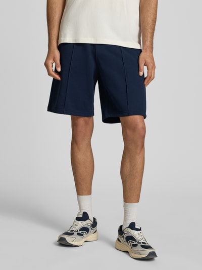 Männermodel trägt Bermudas mit elastischem Bund und Label-Stitching von CHAMPION aus Baumwoll-Mix, Regular-Fit, Längsnähte, Nahaufnahme Oberkörper.