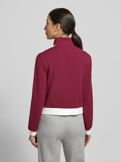 Frauenmodel trägt Regular Fit Sweatjacke mit Stehkragen von Marc Cain in Bordeaux mit weißen Details, elastischer Material-Mix, Ganzkörperansicht Rückansicht.