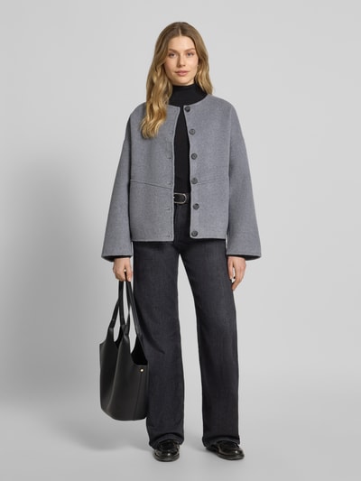 Modelka kobieca ma na sobie Loose Fit Jacke aus Woll-Mix Modell 'EDDY' od SUNCOO PARIS, szary, okrągły dekolt, guziki, długość tyłu w rozmiarze S: 65 cm, szerokość ramion w rozmiarze S: 64 cm, szerokość klatki piersiowej w rozmiarze S: 65 cm, długość rękawa w rozmiarze S: 48 cm, pełny widok z przodu.