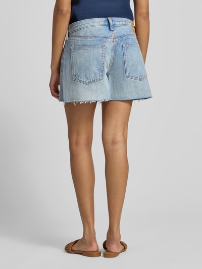 Modelka nosi Relaxed Fit Bermudas aus reiner Baumwolle von Polo Ralph Lauren, jasnoniebieski denim, długość cropped, frędzle, łatka z logo, 5 kieszeni, zapięcie na guzik i ukryty zamek, szlufki na pasek, boczne rozcięcie, materiał: czysta bawełna. Widok całej sylwetki z tyłu.